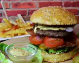Soczysty burger z wołowiny, bekonem, warzywami i frytkami w tle.