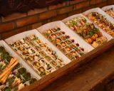 Elegancki catering do domu: pięknie ułożone przekąski w kartonowych pudełkach, od mini kanapek po rolki z łososiem i warzywami.