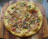 Pyszna pizza bianca z szynką, serem i zielonymi dodatkami, posypana przyprawami, na drewnianej desce.