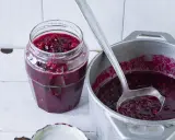 Słoik z konfiturą żurawinową i chochla w garnku z konfiturą.