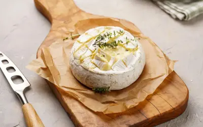 Pyszny camembert z grilla, zapieczony z ziołami, na drewnianej desce. Idealny do maczania.