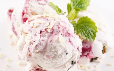 Pyszne lody z mascarpone z malinową nutą i chrupiącymi kawałkami białej czekolady, ozdobione listkiem mięty.