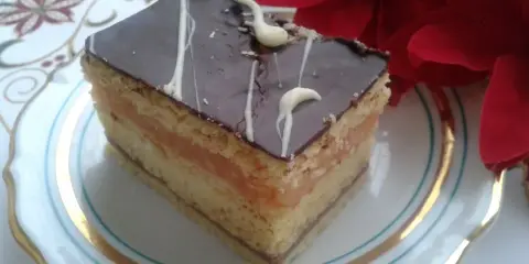 Pyszny kawałek ciasta z warstwami biszkoptu, kremu serowego i jabłek, oblany czekoladą. Idealny na przepis na ciasto delicja z serem i jabłkami.