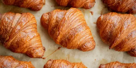 Złociste, chrupiące rogaliki ułożone na papierze do pieczenia. Idealne na śniadanie, choć warto pamiętać o ich kaloryczności – croissant kcal.