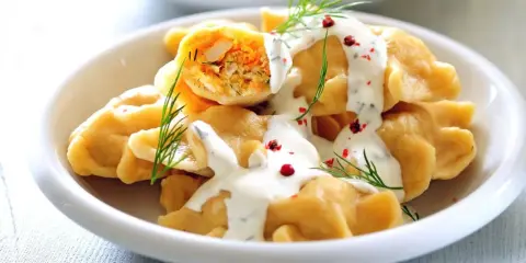 Pyszne pierogi z farszem, polane sosem i posypane koperkiem. Idealne danie, by zastanowić się, co ugotować w piątek na obiad.