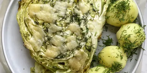 Pieczona młoda kapusta z serem i koperkiem, podana z młodymi ziemniakami. Idealny pomysł, co zrobić z młodej kapusty na obiad.