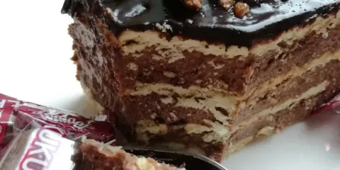 Czekoladowe ciasto bez pieczenia z wafli, idealne na przepis na ciasto kukułka bez pieczenia. Na wierzchu błyszcząca polewa i orzechy.