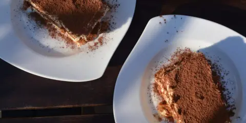 Dwa kawałki tiramisu posypane kakao na białych talerzach. Idealne do mocnej kawy, która podkreśli smak.