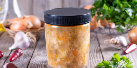 Słoik z domową zupą warzywną, obok cebula, czosnek i chili. Dowiedz się, jakich zup nie można mrozić.