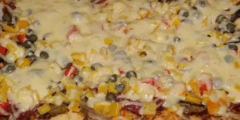 Pyszna pizza na grubym cieście z warzywami i roztopionym serem.