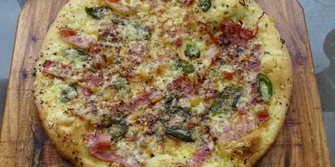 Pyszna pizza bianca z szynką, serem i zielonymi dodatkami, posypana przyprawami, na drewnianej desce.