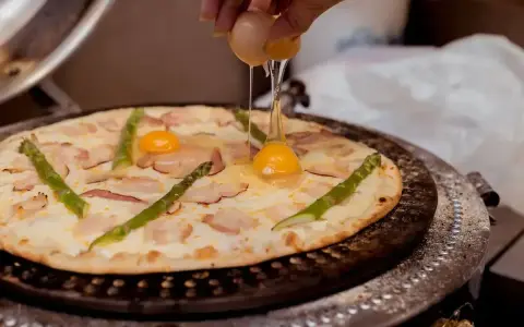 Pizza z jajkiem i szparagami, na którą wylewane jest surowe jajko.
