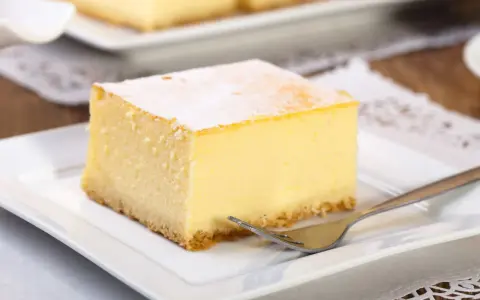 Pyszny sernik z wiaderka, idealny do pieczenia w temperaturze 170°C. Pokrojony na kwadratowe porcje, posypany cukrem pudrem, czeka na widelczyk.