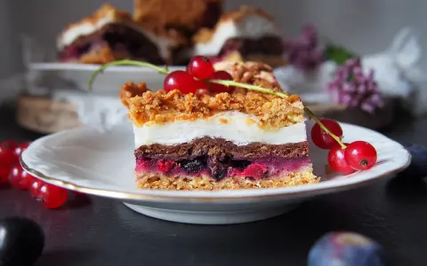 Pyszny kawałek ciasta pleśniak z dżemem porzeczkowym, ozdobiony świeżymi porzeczkami. Idealny na deser.