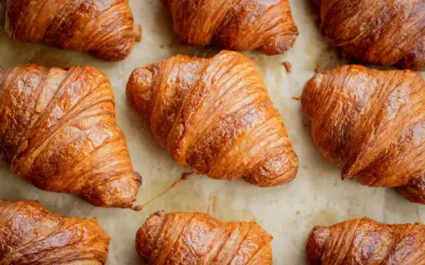 Złociste, chrupiące rogaliki ułożone na papierze do pieczenia. Idealne na śniadanie, choć warto pamiętać o ich kaloryczności – croissant kcal.