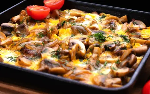 Pyszne danie z pieczarkami i jajkiem zapieczone w naczyniu, ozdobione pomidorkami i koperkiem. Idealne co z pieczarkami na obiad!