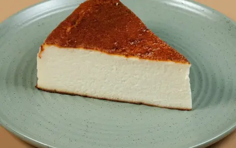 Pyszny kawałek sernika pieczonego bez spodu, z lekko przypieczoną górą, na zielonym talerzu.