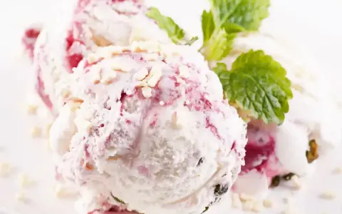 Pyszne lody z mascarpone z malinową nutą i chrupiącymi kawałkami białej czekolady, ozdobione listkiem mięty.