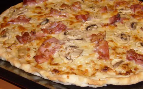 Pyszna pizza carbonara z chrupiącym boczkiem, pieczarkami i ciągnącym się serem. Idealna na szybki obiad.