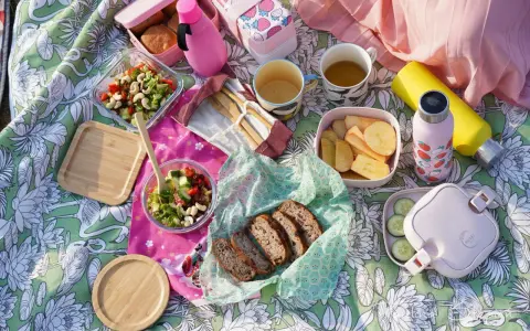Piknikowy koc z jedzeniem: sałatki, chleb, owoce, napoje i bambuowe sztućce.