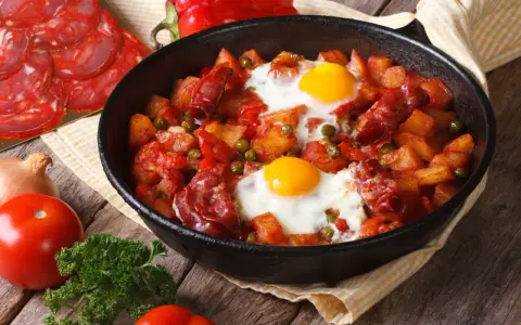 Pyszne danie z jajek na obiad: ziemniaki, chorizo, papryka i groszek zapiekane w patelni.