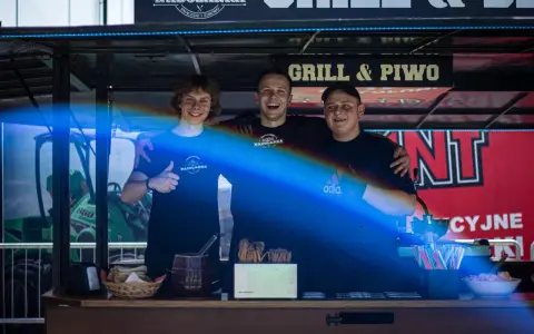 Trzech uśmiechniętych mężczyzn za ladą cateringową z napisem "Grill & Piwo".