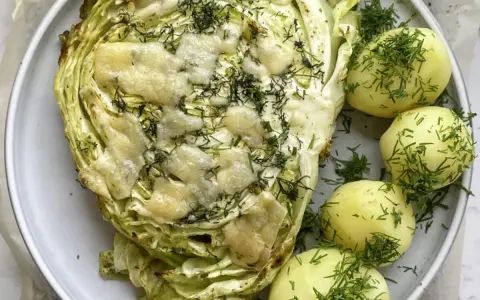 Pieczona młoda kapusta z serem i koperkiem, podana z młodymi ziemniakami. Idealny pomysł, co zrobić z młodej kapusty na obiad.