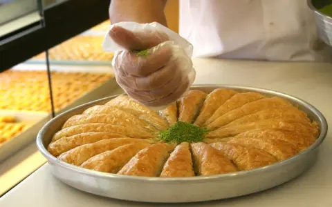 Słodka baklava, co to za przysmak? Warstwy ciasta filo, orzechy i syrop. Posypka z pistacji dodaje uroku.