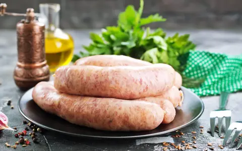 Świeża kiełbasa na talerzu, obok przyprawy i ziół. Zastanawiasz się, jak długo można mrozić kiełbasę?