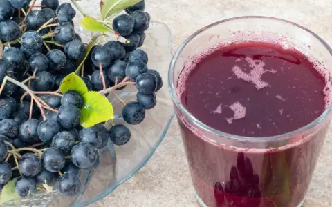 Świeża aronia na talerzu i szklanka soku. Idealne do przygotowania przetworów, np. jak mrozić aronię na zimę.