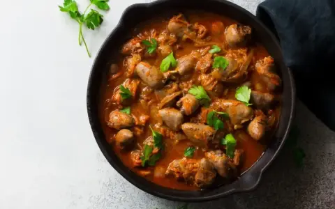 Serca drobiowe w gęstym, aromatycznym sosie, udekorowane świeżą natką pietruszki, podane w żeliwnej patelni.