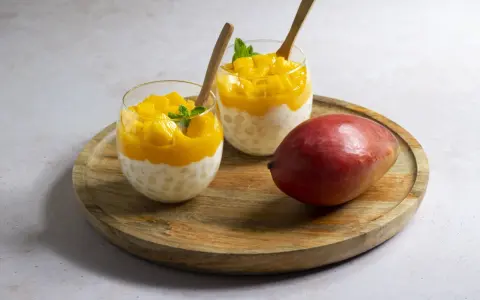 Pyszny deser z tapioki i mango, idealny sposób, by wykorzystać mrożone mango. Podany w szklankach z drewnianymi łyżeczkami.