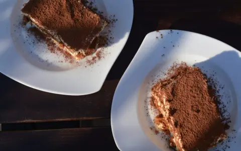 Dwa kawałki tiramisu posypane kakao na białych talerzach. Idealne do mocnej kawy, która podkreśli smak.