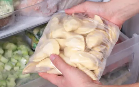Ręce wkładają do zamrażarki worek z pierogami. To prosty sposób, jak mrozić pierogi, by cieszyć się nimi później.