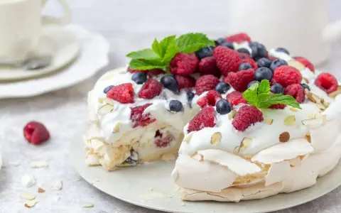 Beza Pavlova która zawsze wychodzi, udekorowana bitą śmietaną, malinami, borówkami i listkami mięty. Idealna na deser.