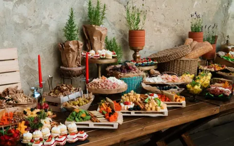 Bogaty stół z serami, owocami, ciastkami i pieczywem. Idealny na przyjęcie, zastanawiasz się, ile kosztuje catering na 15 osób?