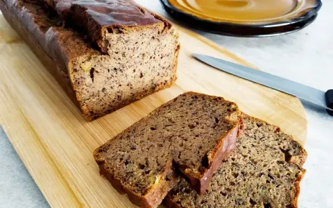 Wilgotny chleb bananowy pokrojony na desce, obok nóż i talerz.