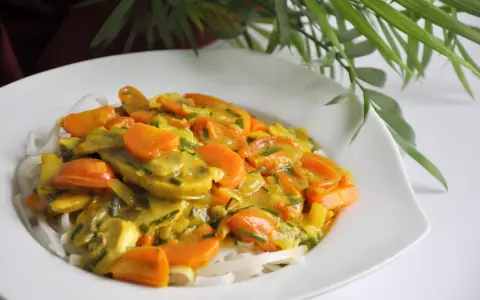 Zdrowy obiad: makaron ryżowy z warzywami w sosie curry. Kolorowe marchewki i inne warzywa tworzą apetyczną kompozycję.