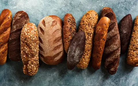 Różnorodne rodzaje chleba: bagietki, bochenki z ziarnami i ciemne pieczywo ułożone na niebieskim tle.