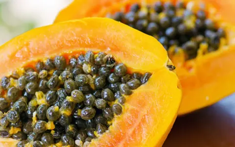 Dwa soczyste kawałki papaya z mnóstwem czarnych nasion w środku.