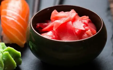 Miseczka z marynowanym imbirem do sushi, obok kawałka sushi z łososiem i wasabi.