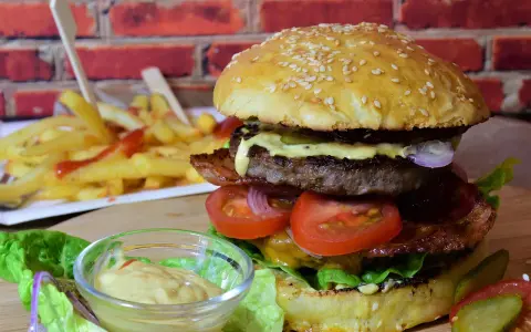 Soczysty burger z wołowiny, bekonem, warzywami i frytkami w tle.