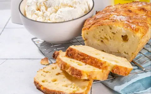 Wilgotny bochenek z twarogiem, pokrojony na kromki, obok miski z twarogiem.