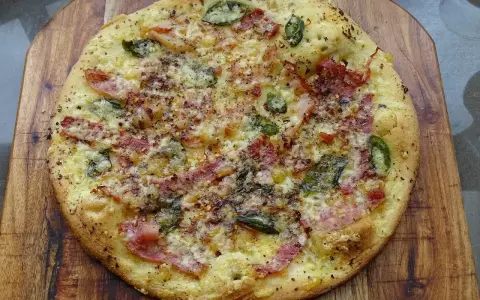 Pyszna pizza bianca z szynką, serem i zielonymi dodatkami, posypana przyprawami, na drewnianej desce.