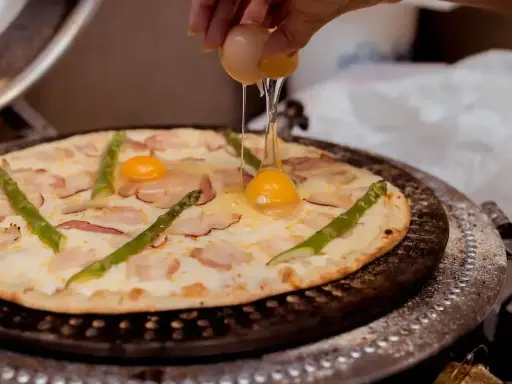 Pizza z jajkiem i szparagami, na którą wylewane jest surowe jajko.