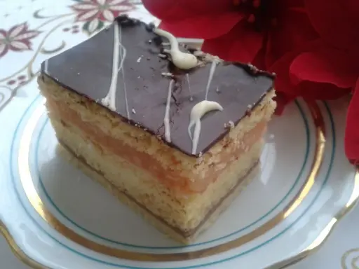 Pyszny kawałek ciasta z warstwami biszkoptu, kremu serowego i jabłek, oblany czekoladą. Idealny na przepis na ciasto delicja z serem i jabłkami.