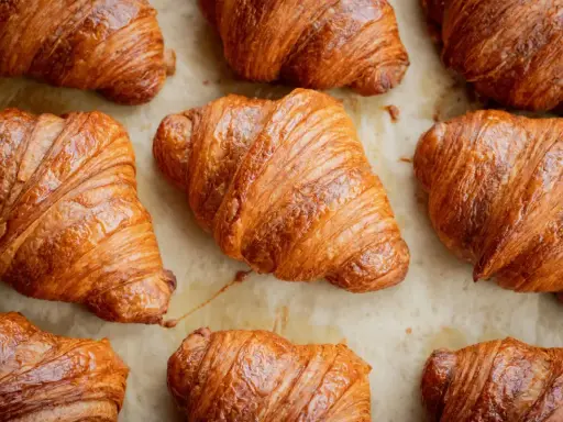Złociste, chrupiące rogaliki ułożone na papierze do pieczenia. Idealne na śniadanie, choć warto pamiętać o ich kaloryczności – croissant kcal.