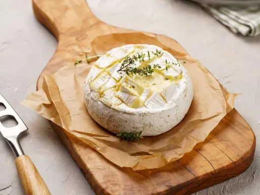Pyszny camembert z grilla, zapieczony z ziołami, na drewnianej desce. Idealny do maczania.