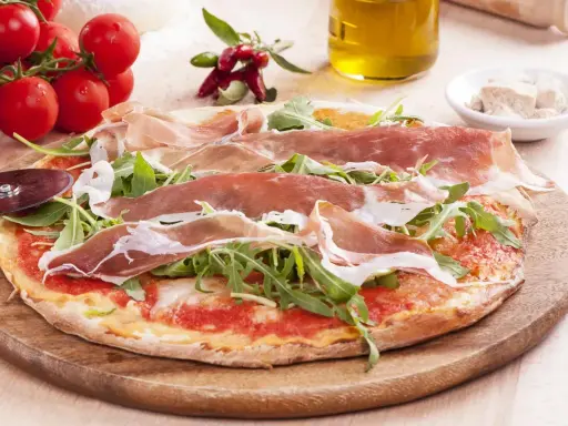 Pyszna pizza prosciutto z rukolą, pomidorkami i oliwą. Idealna na włoską ucztę.