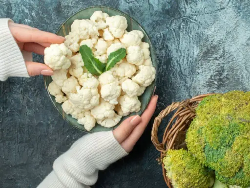 Ręce trzymające różyczki kalafiora nad talerzem, obok koszyk z brokułami. Zastanawiasz się, czy można mrozić kalafior? Tak, można!